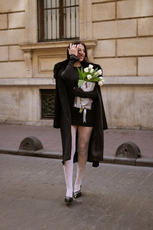 A Fashionable Woman Standing on a Sidewalk with a Bunch of Flowers 