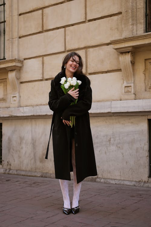 A woman in black coat and white stockings holding flowers
