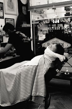A vintage-style shot of a barber preparing to shave a customer in a traditional barbershop.