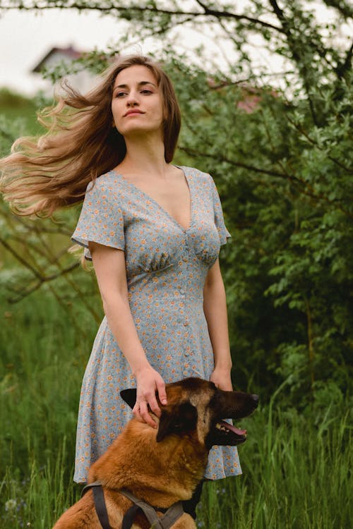 A woman in a dress and a dog in the grass