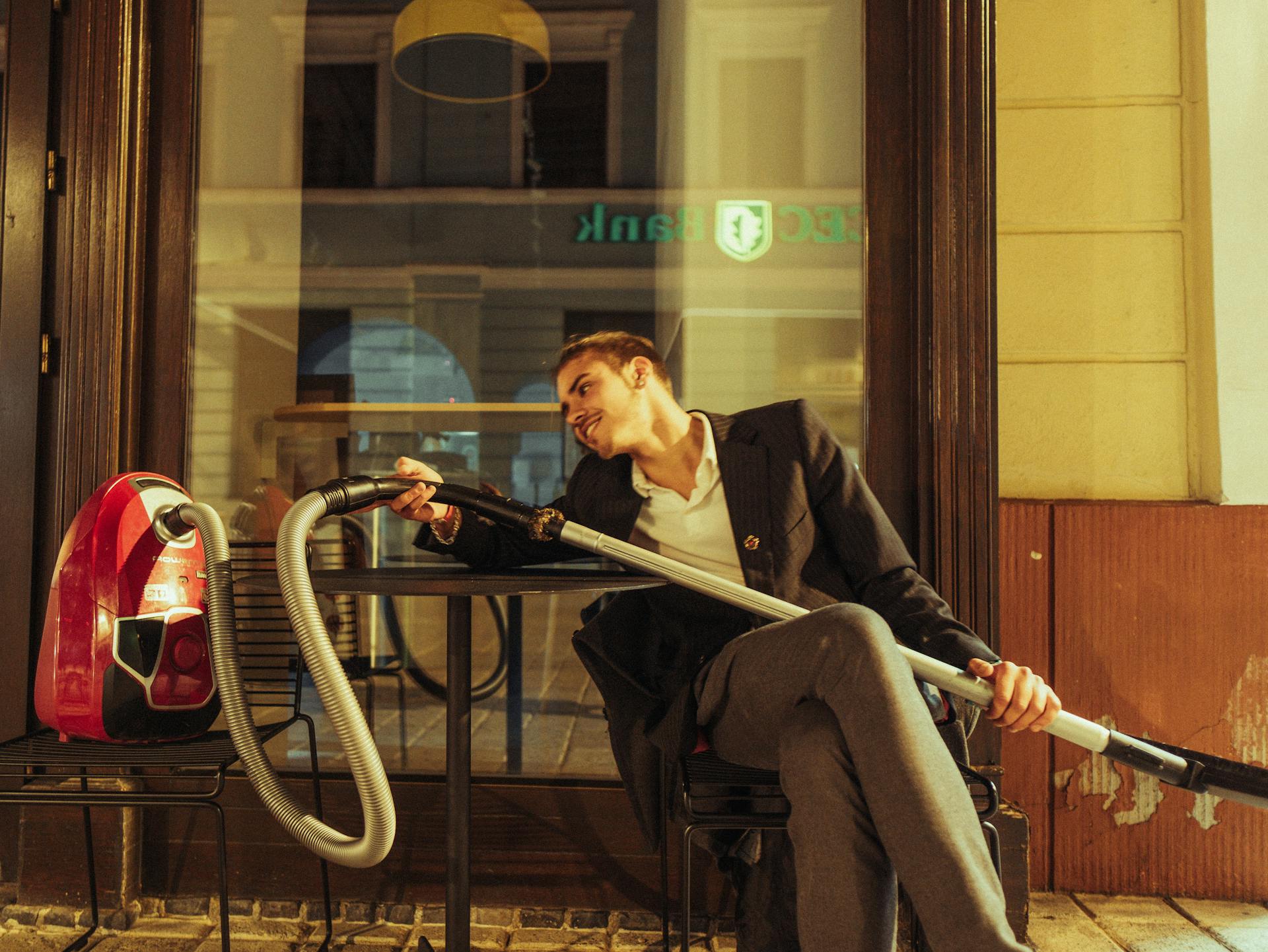 Smiling Man in Suit Sitting with Vacuum Cleaner at Cafe