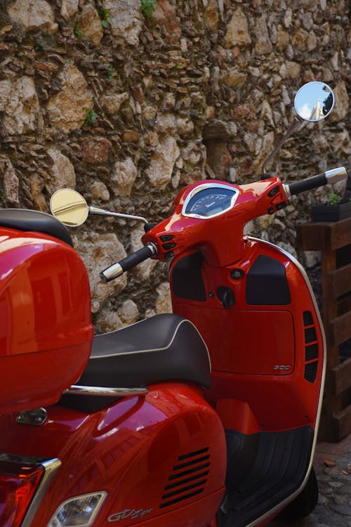 A red scooter parked next to a stone wall