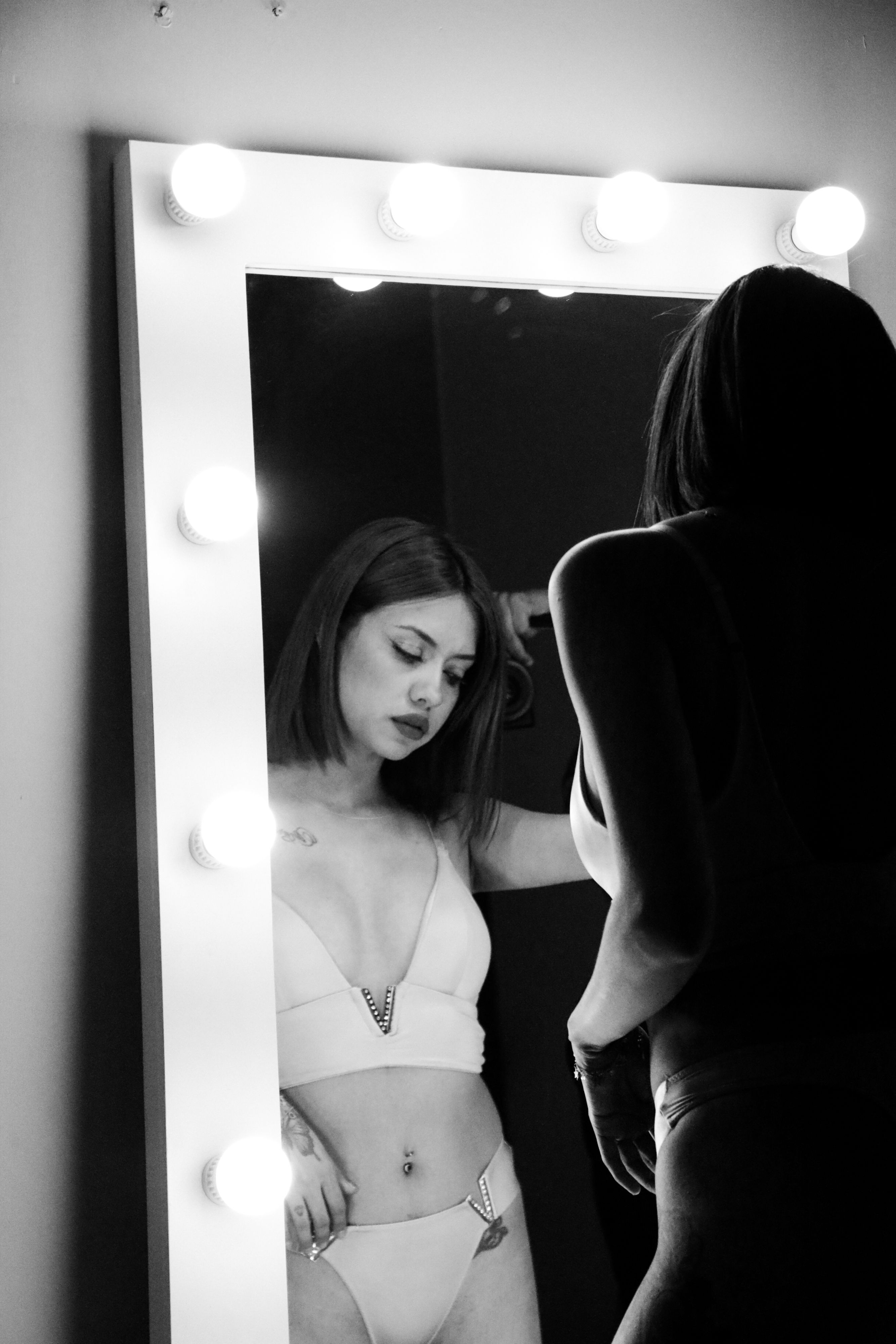 Artistic black and white photo of a woman in lingerie reflecting in a lighted mirror.