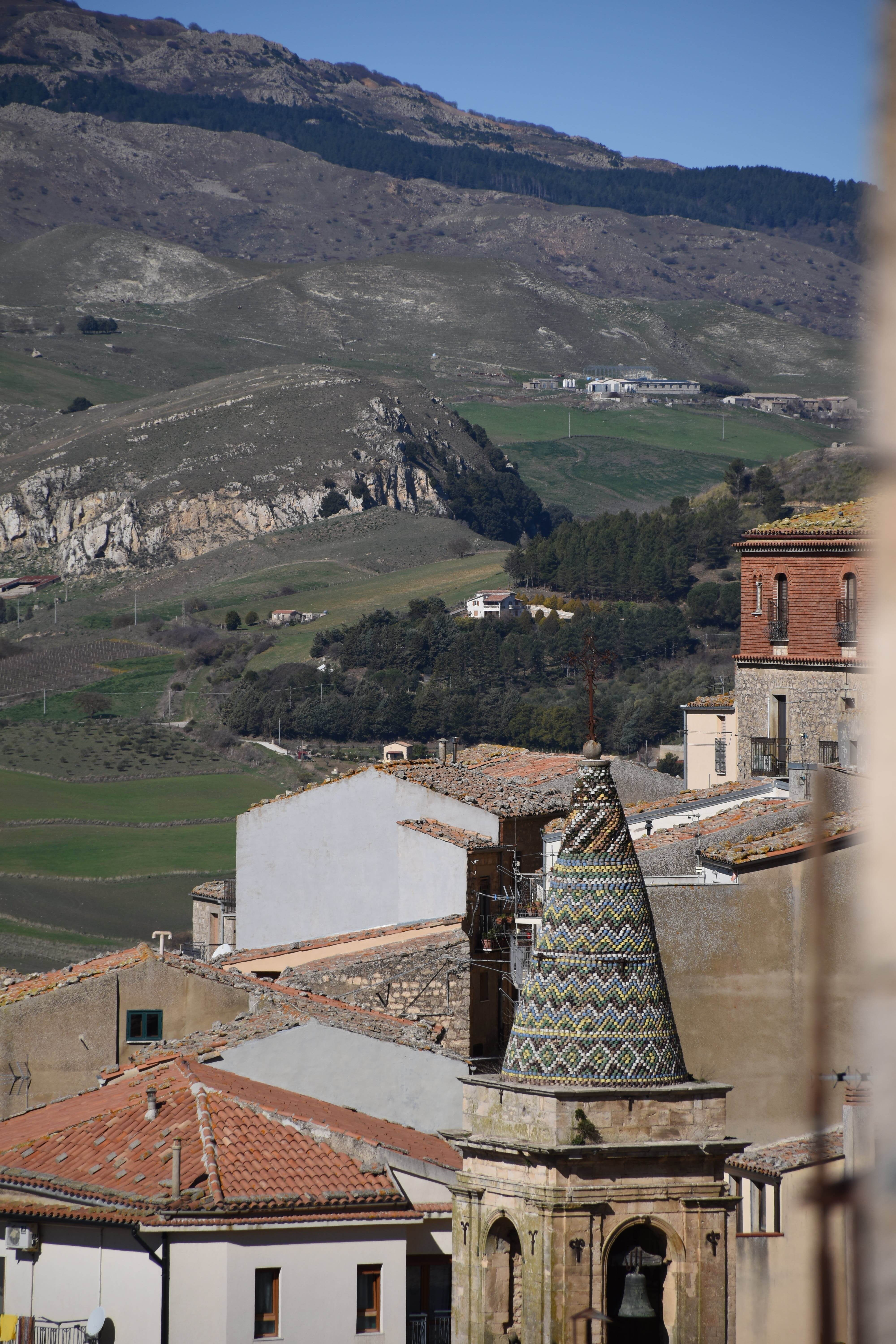 A scenic view of Gangi, Sicily, showcasing historic towers and lush countryside.