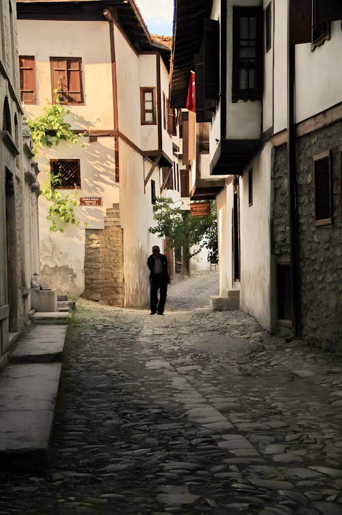 Candid Photo of a Pedestrian Walking on a Cobblestone Street between Ottoman Houses