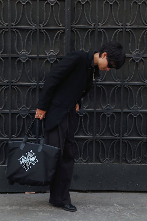 Man in Black Suit and with Bag Bending near Wall