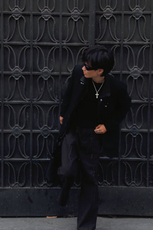 A man in black clothes and sunglasses standing in front of a black gate