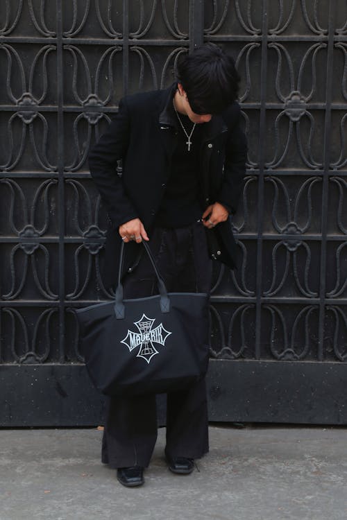 A man in black jacket and pants holding a black tote bag