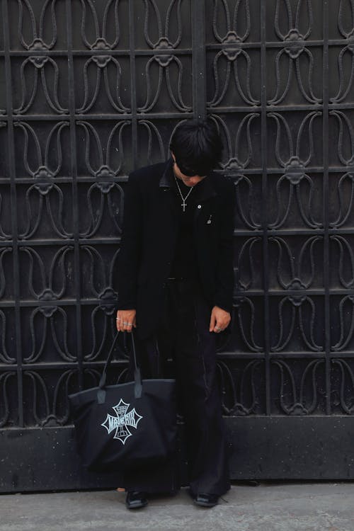 A person standing in front of a black gate with a black bag
