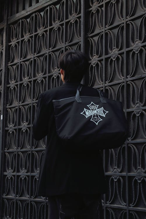 A man with a black bag walks by a metal gate