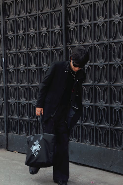 A man in black pants and a black jacket carrying a bag