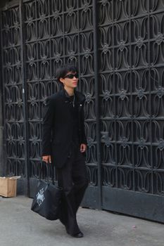Fashionable man in sunglasses walking on a city street with a designer bag and coat.