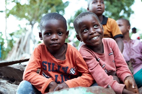 Two young children sitting on the ground and smiling