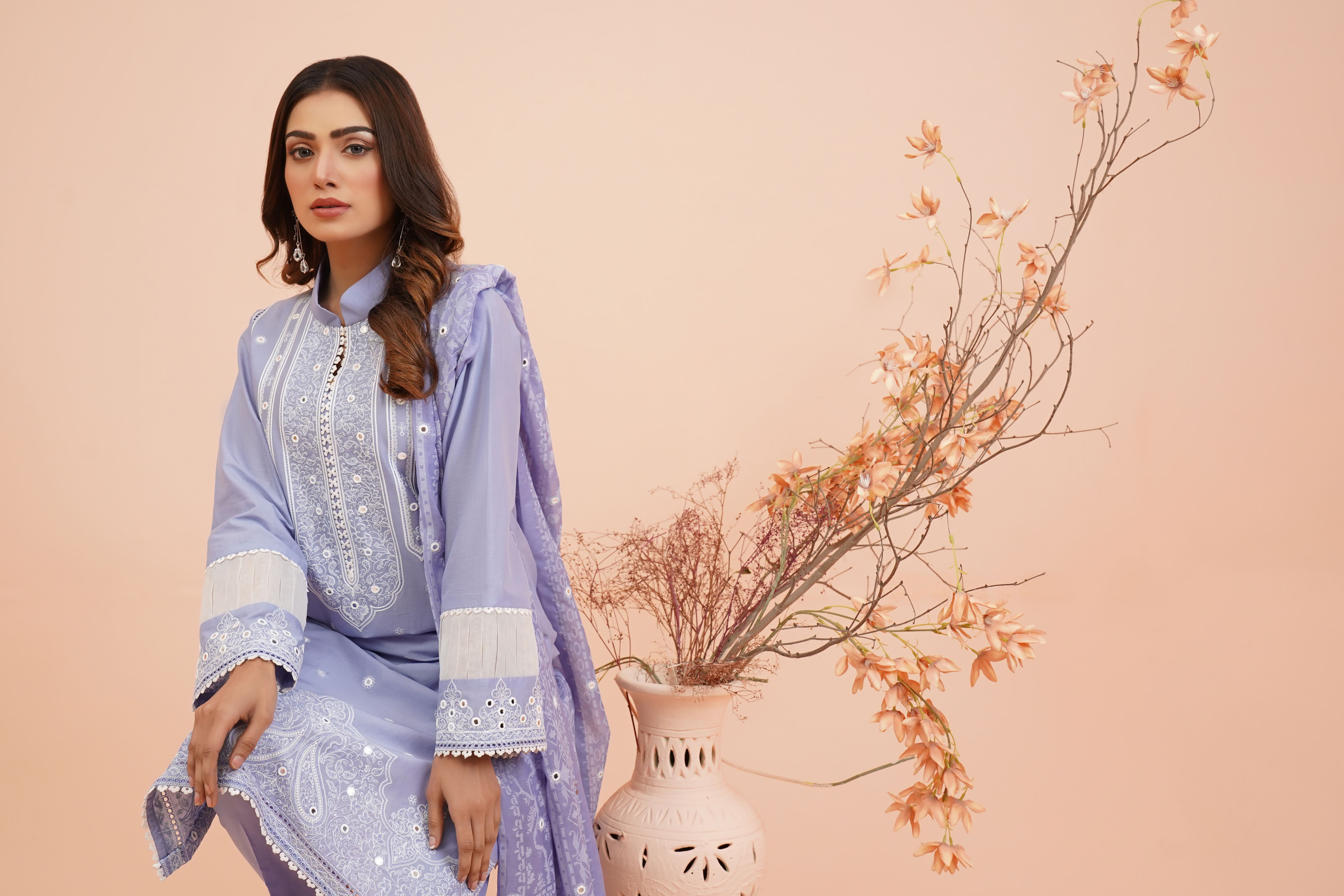 A woman in a light pastel embroidered lawn dress with delicate floral patterns, showcasing Pakistani craftsmanship