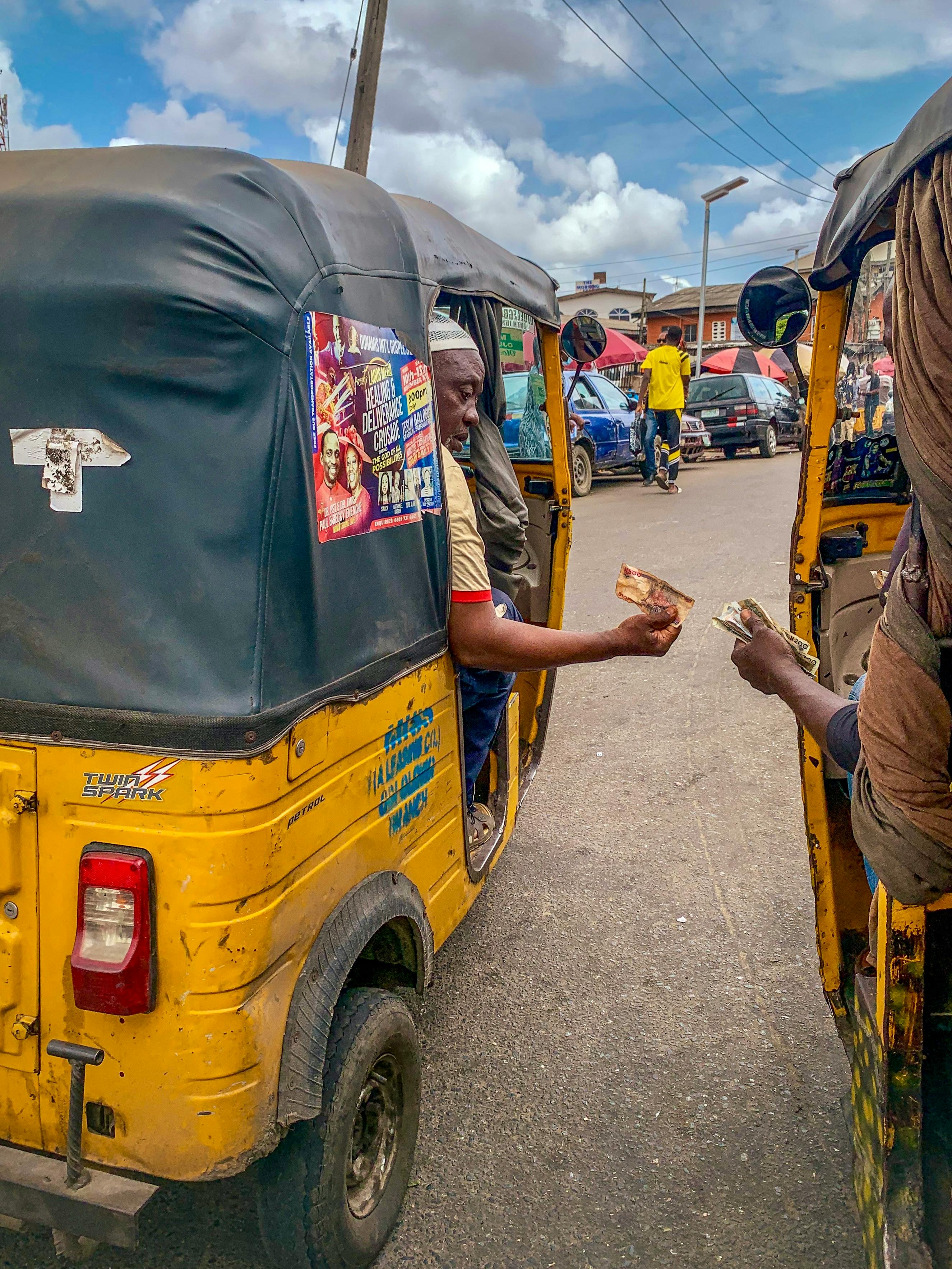 Vibrant city street scene with people exchanging items in yellow rickshaws.