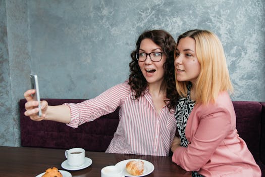 Two women enjoy coffee and pastries while taking a selfie in a cozy café.