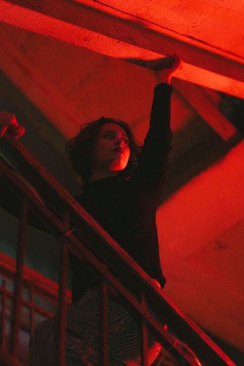 Free Artistic photo of a woman in red light, raising an arm above a stairway. Stock Photo