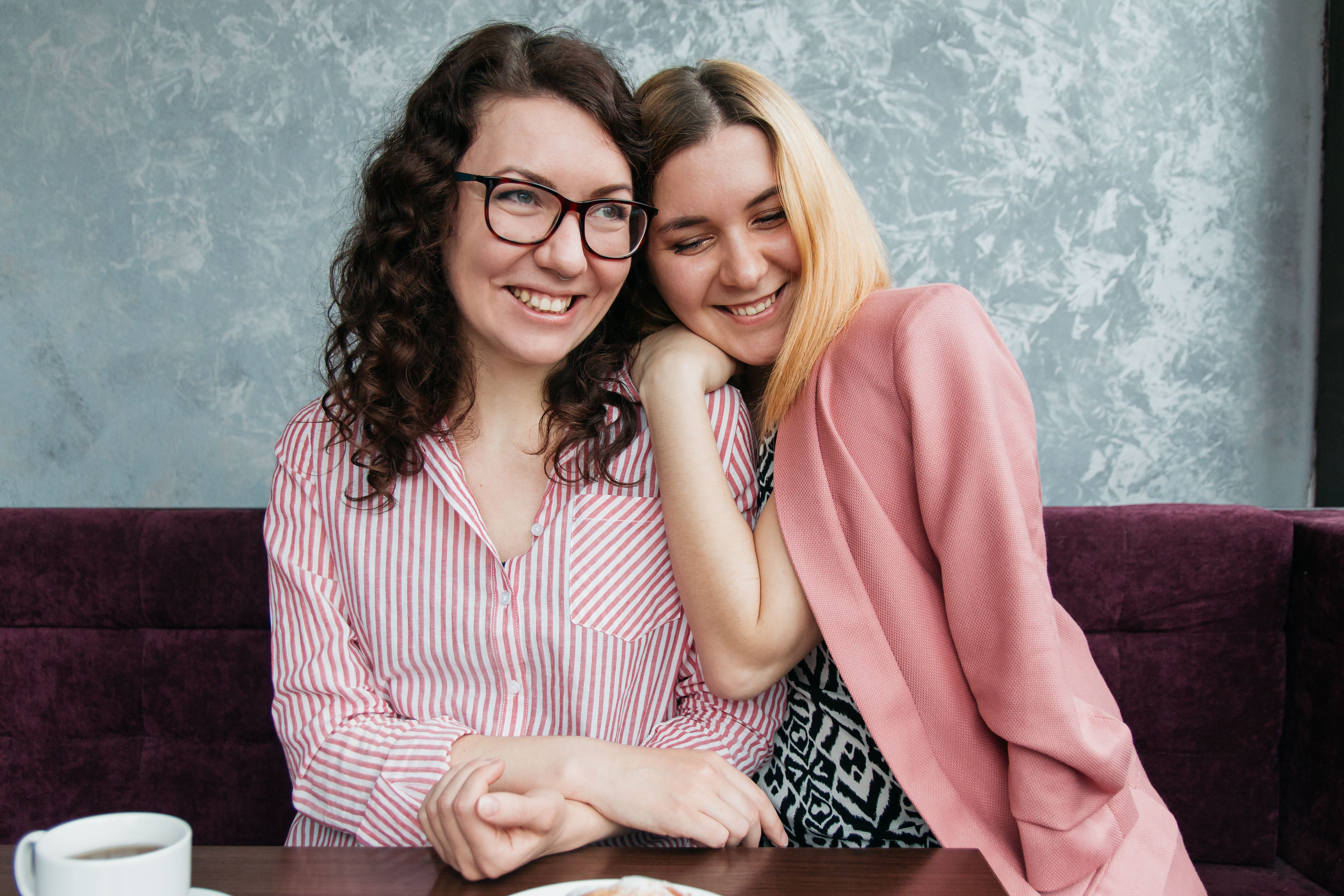 Two women enjoying a warm moment and sharing smiles inside a cozy café setting.