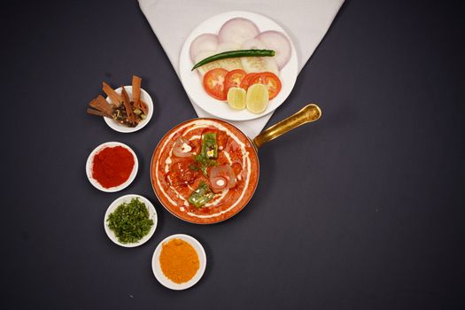 Overhead shot of Indian curry with spices and fresh vegetables on dark background.