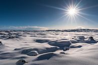 Captivating snowy scene in Iceland with bright sun and clear blue sky over a vast snowy landscape.