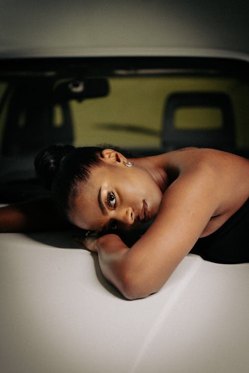 A woman laying on top of a white car
