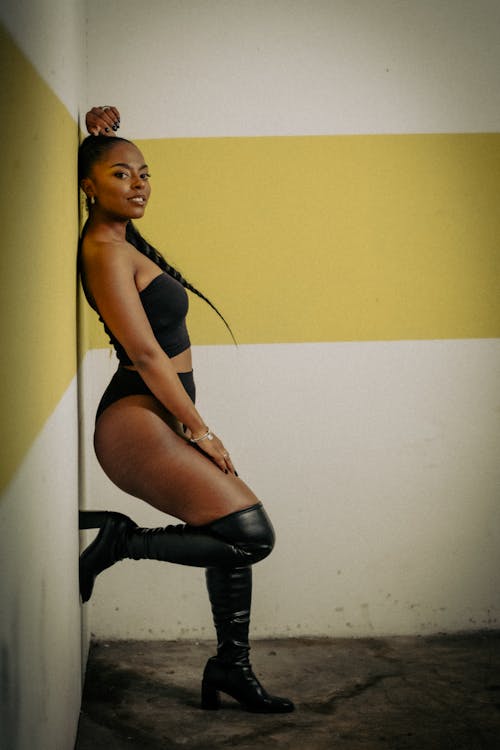 A woman in black thigh high boots leaning against a wall