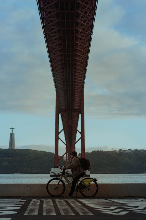 Cyclists Riding on a Lane under the 25 de Abril Bridge in Lisbon, Portugal 