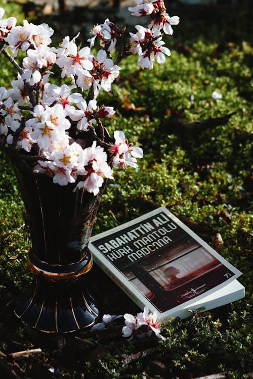 A book and a vase of flowers on the ground