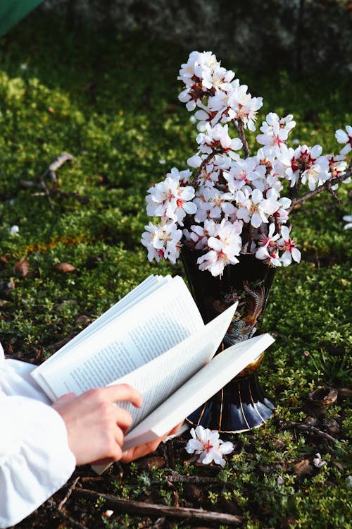 A person reading a book in the grass with flowers