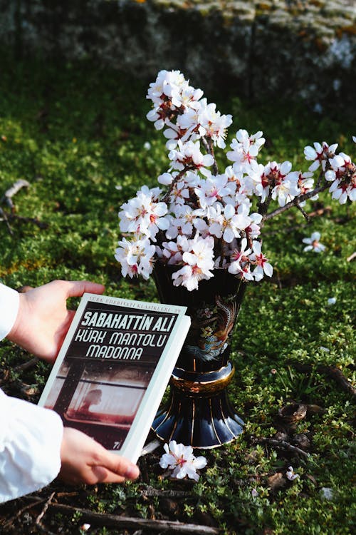A person holding a book in front of a flower