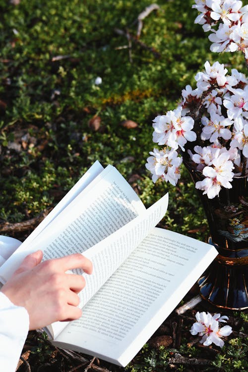 A person reading a book in the grass with flowers