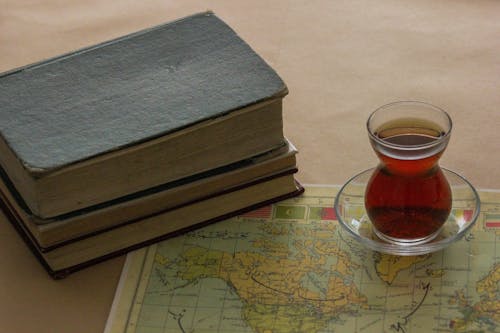 A cup of tea sits on top of a book and map