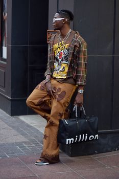 Stylish man in urban streetwear standing on Atlanta sidewalk, showcasing modern fashion.