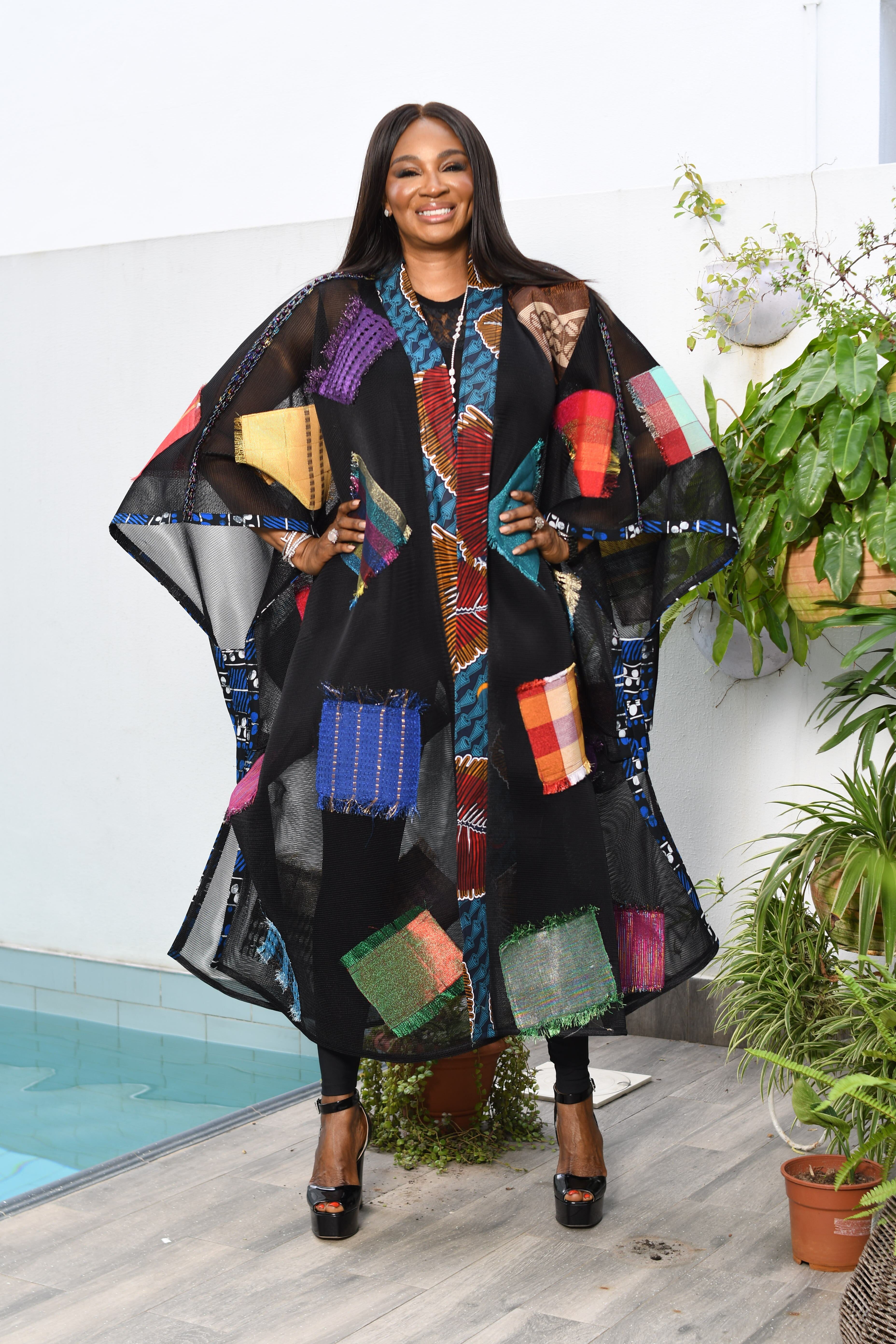 Stylish woman in a colorful patchwork robe standing confidently by a garden indoors.