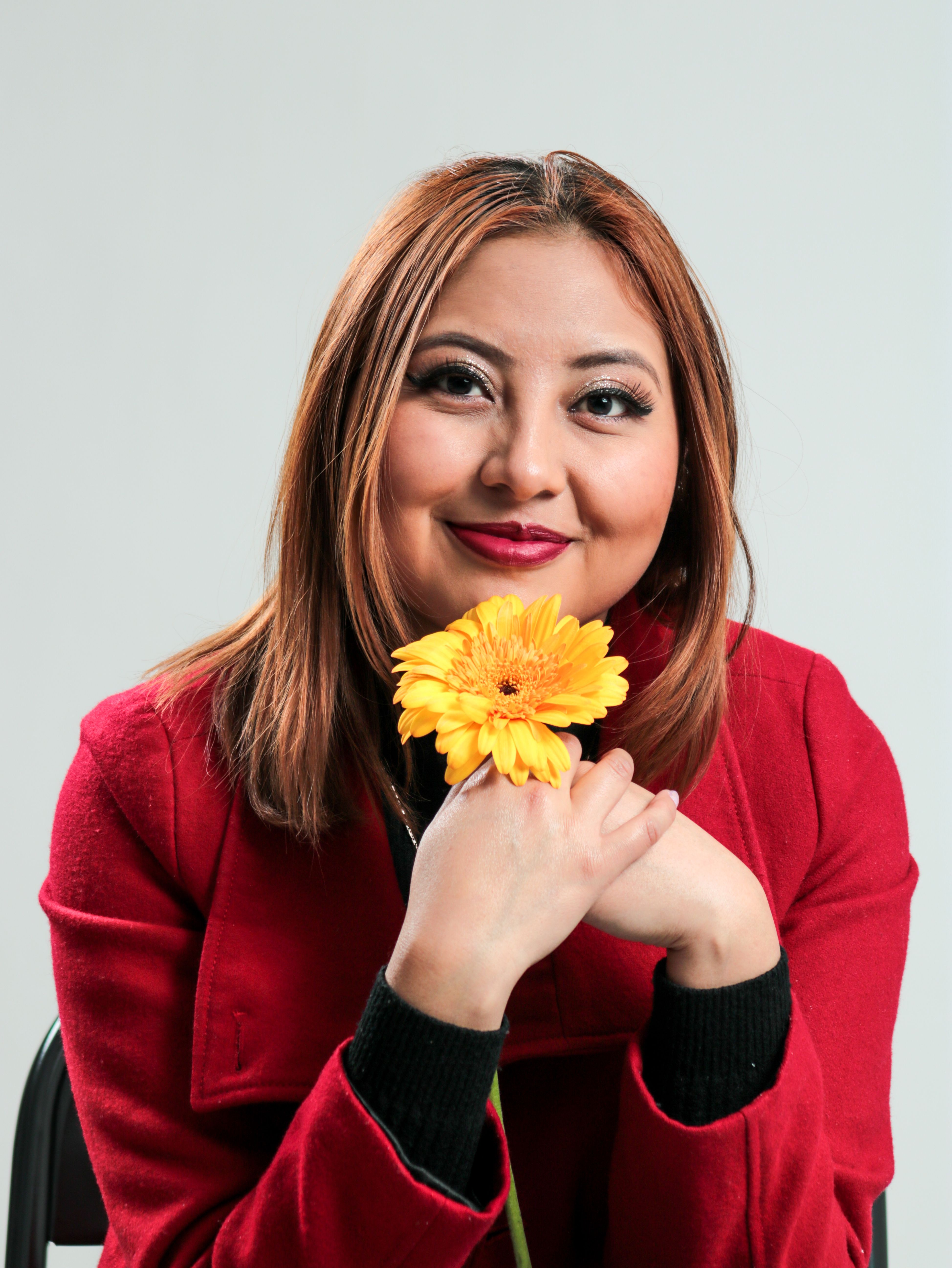 Portrait of a cheerful woman in a red coat holding a yellow flower, smiling.