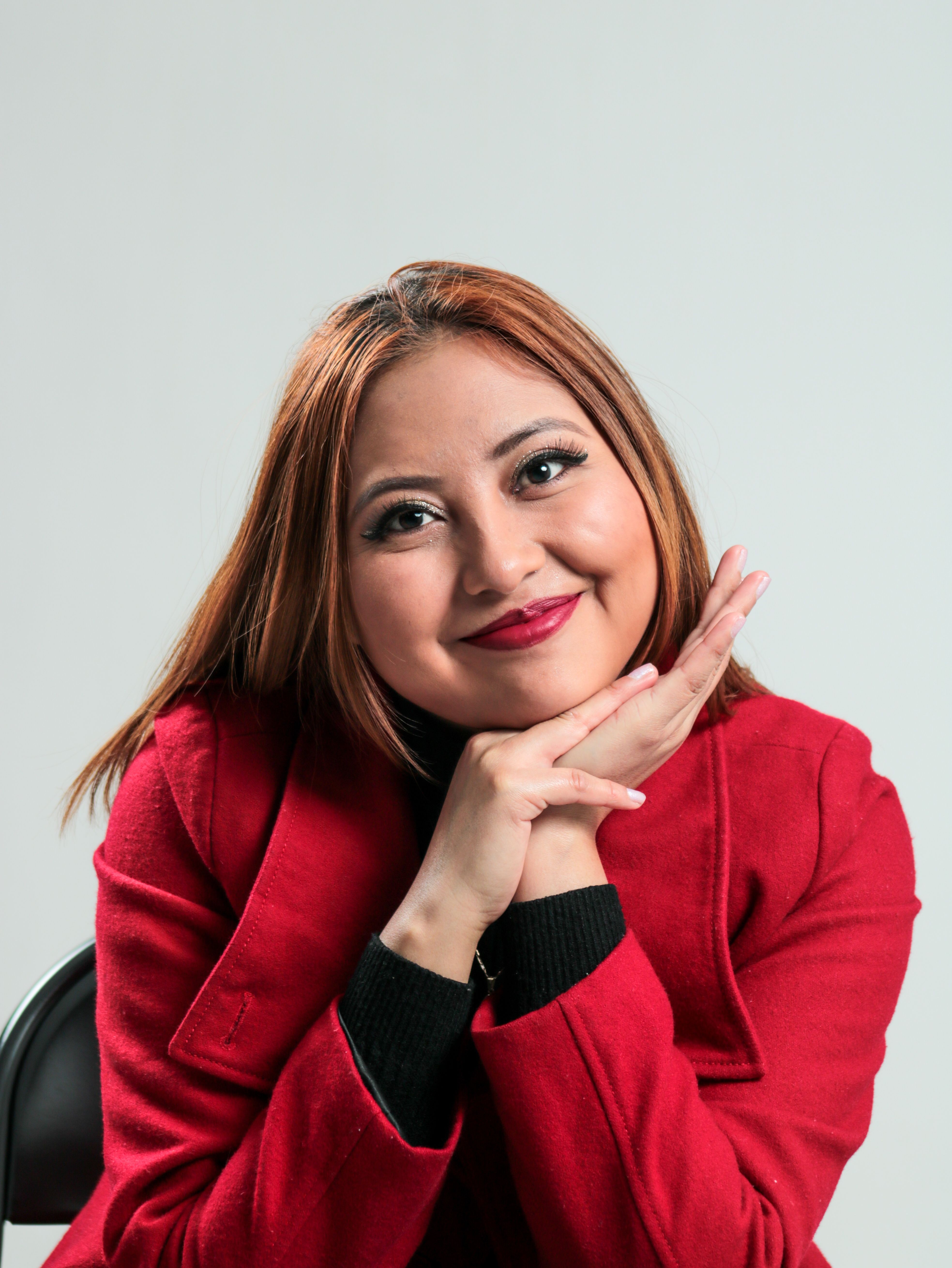 Smiling woman in a red coat posing in a studio setting with a white background.