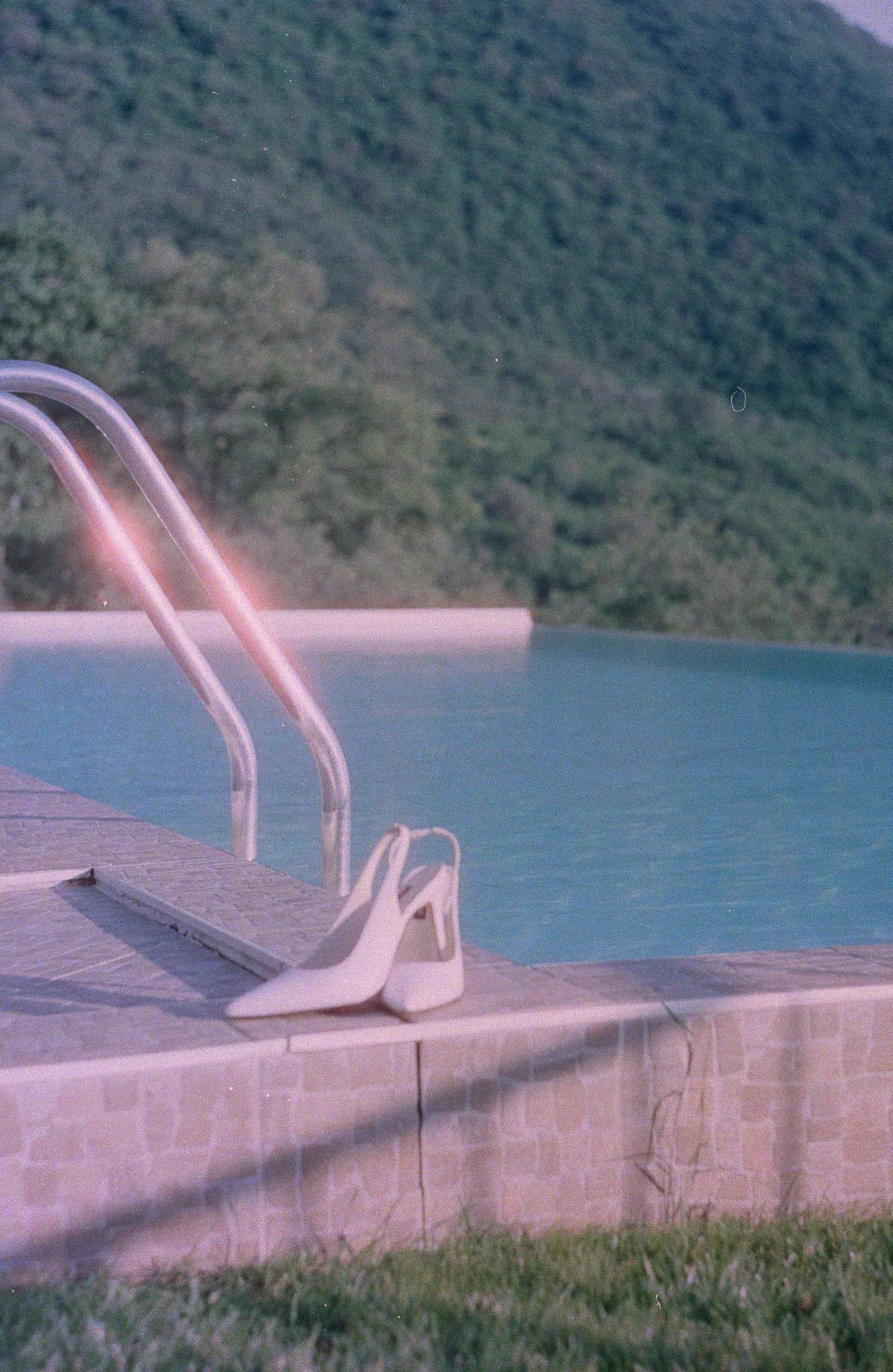White high heel shoe placed by a tranquil swimming pool, exuding summer elegance.