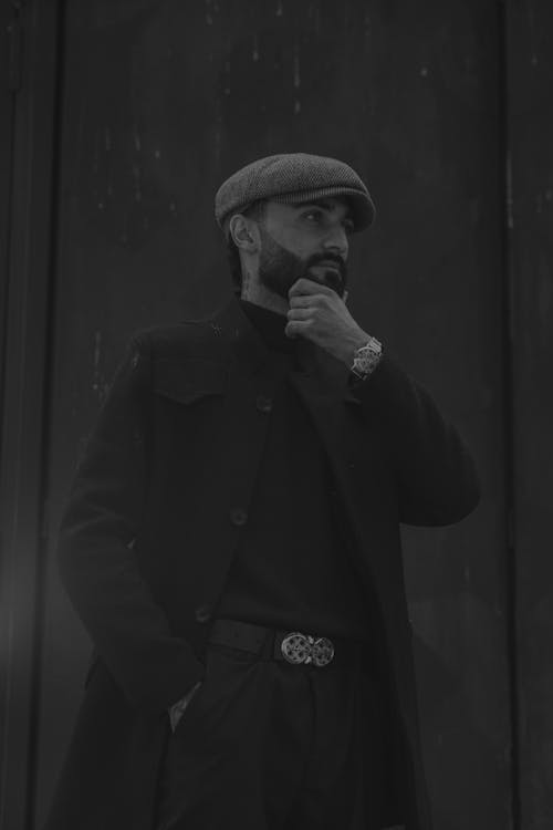 A man in a hat and coat is standing in front of a black and white photo