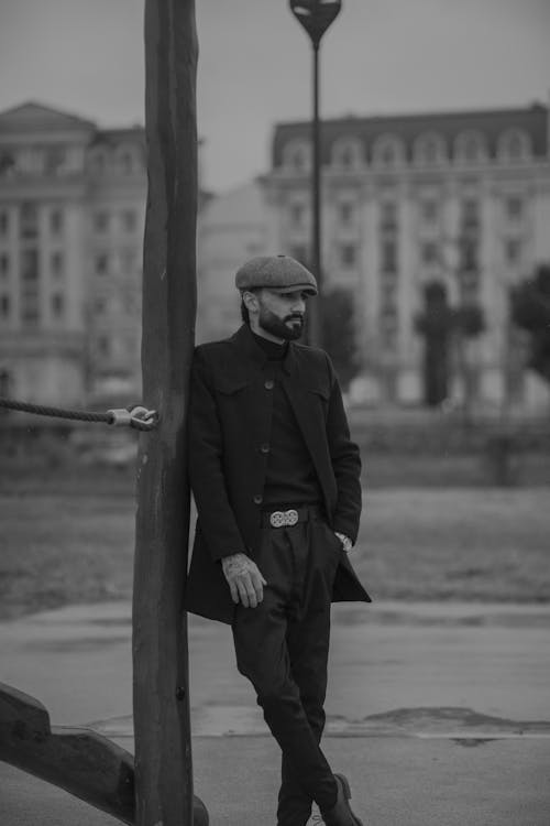 A man in a black coat and hat standing next to a pole