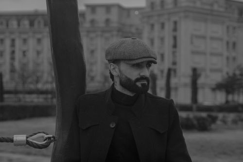 Free Dapper man with beard and cap posing outdoors in grayscale cityscape. Stock Photo