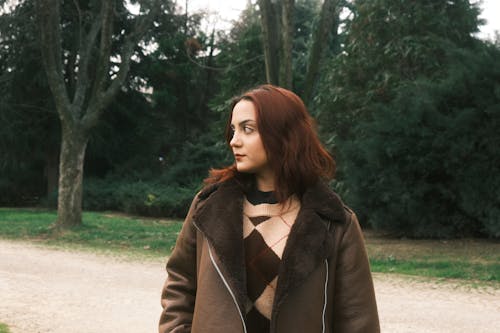 A woman in a brown coat and sweater standing in the woods