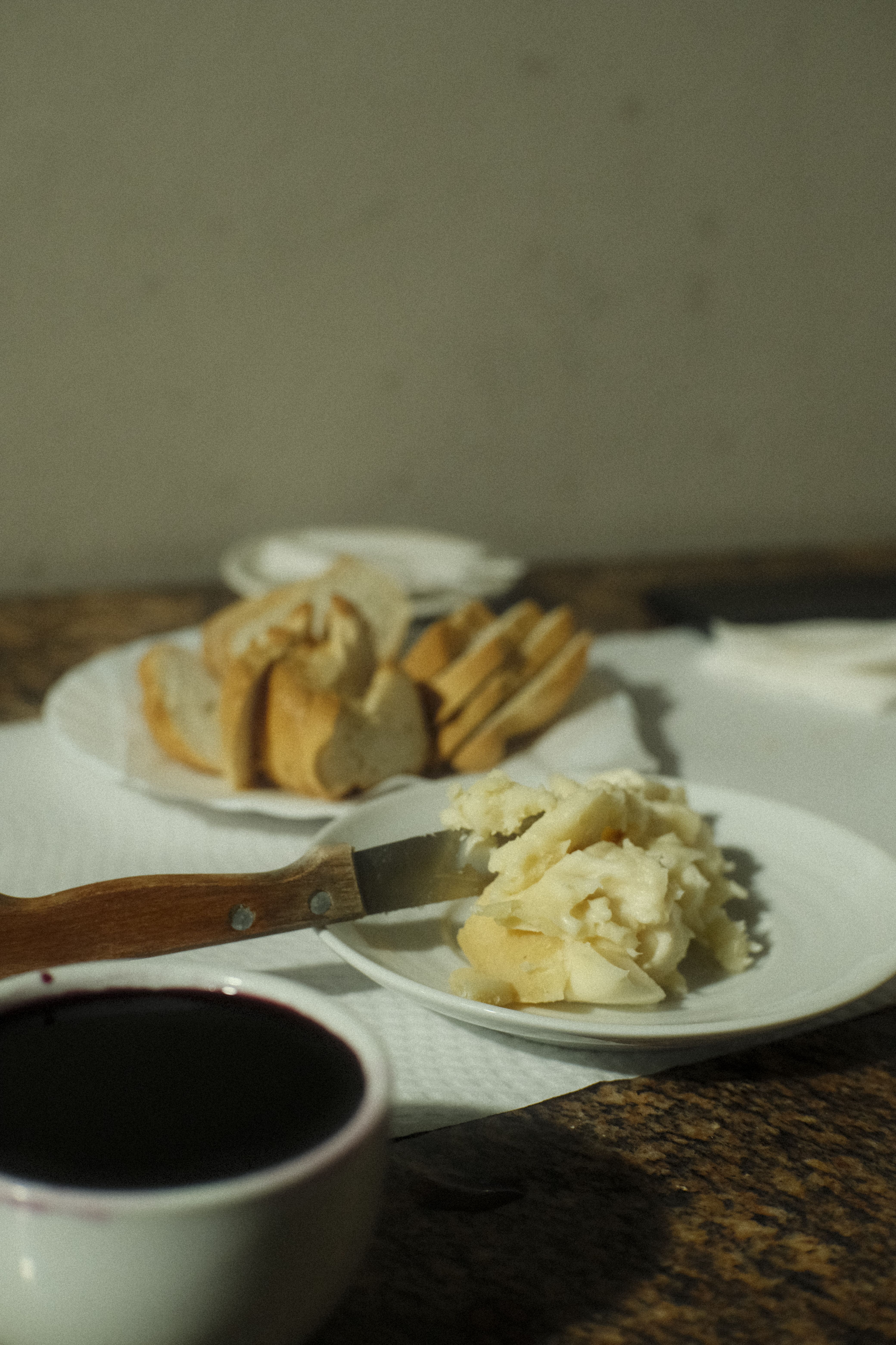 Fotomural Mesa acogedora con pan, queso y vino en una habitación cálida y con poca luz.