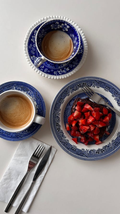 A plate with strawberries and blue cups with coffee