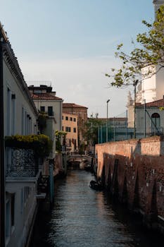 Peaceful Venetian canal in Venecia, Italy, lined by historic buildings and arched bridges under a clear sky.