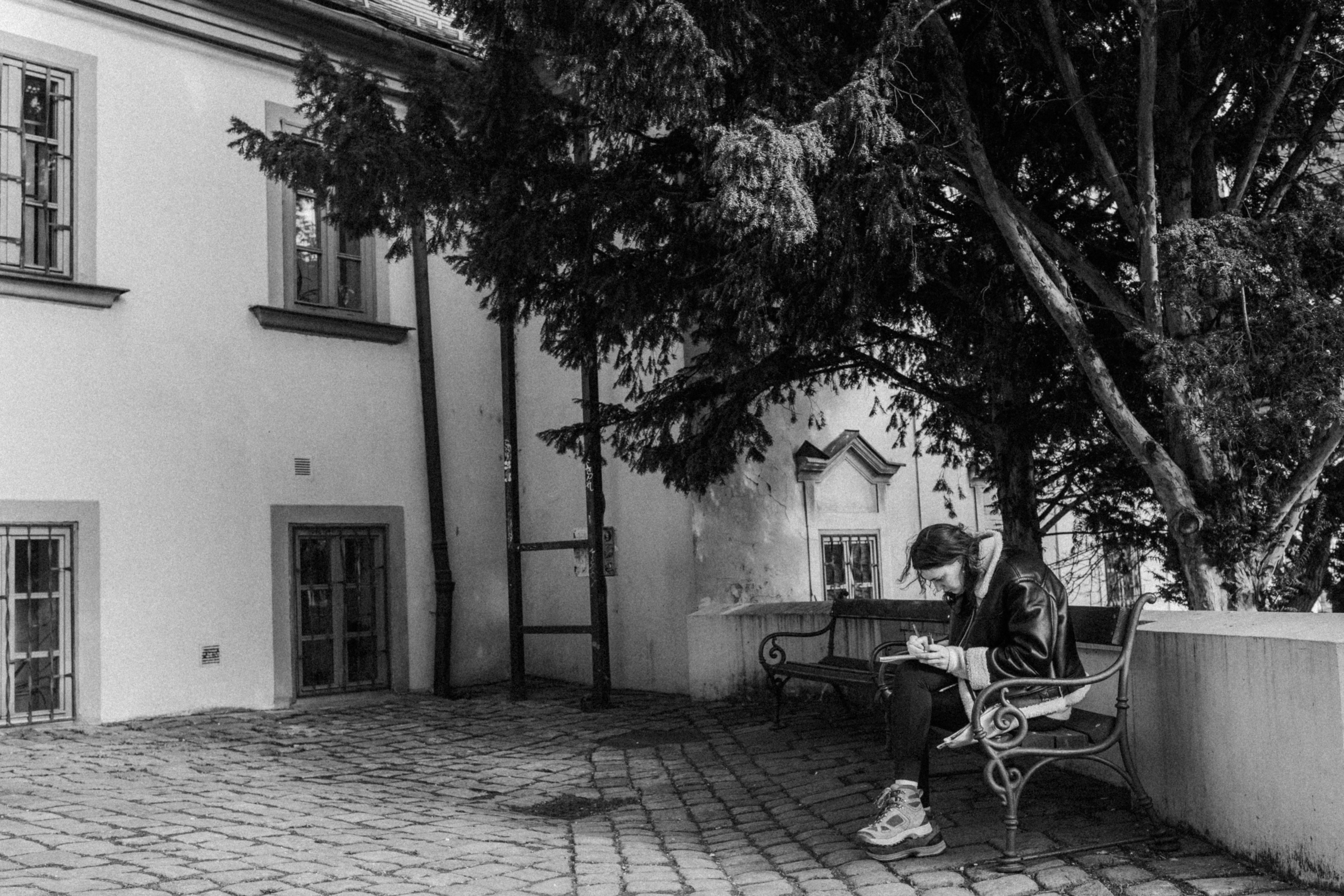A woman sitting on a bench writing in an urban setting in black and white