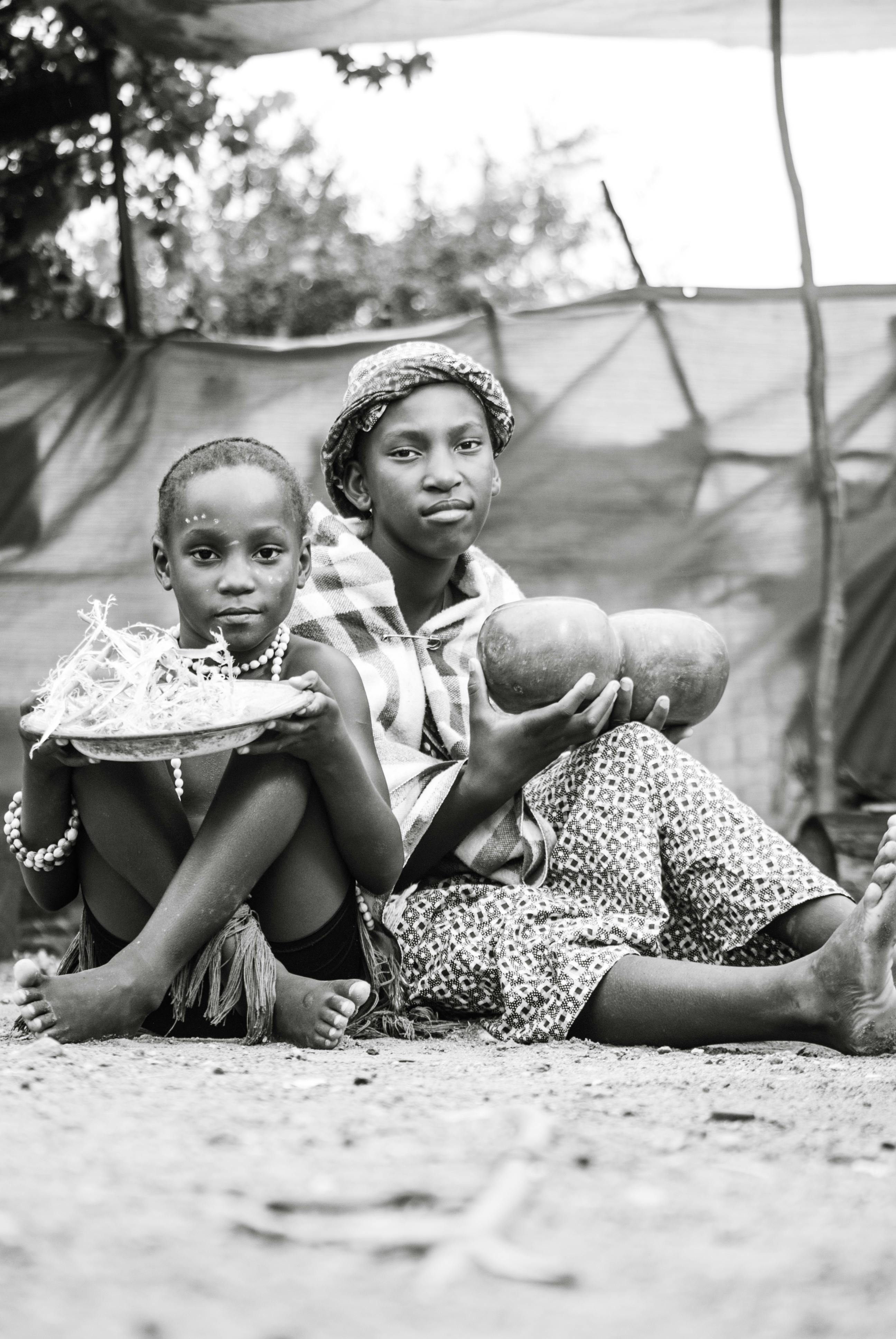 Black and white portrait of an African mother and child sitting outdoors with tribal elements.
