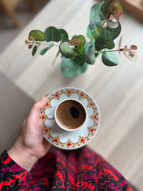 A person holding a cup of coffee in front of a plant