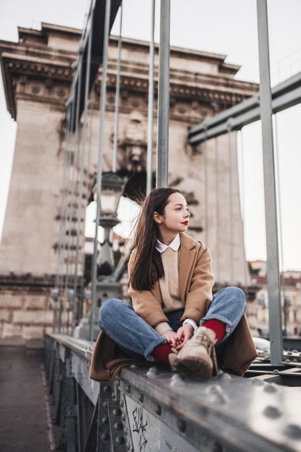 Fashionable woman sitting on a city bridge, showcasing urban style and elegance.