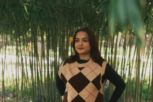 A woman in a brown sweater and black pants standing in front of bamboo trees