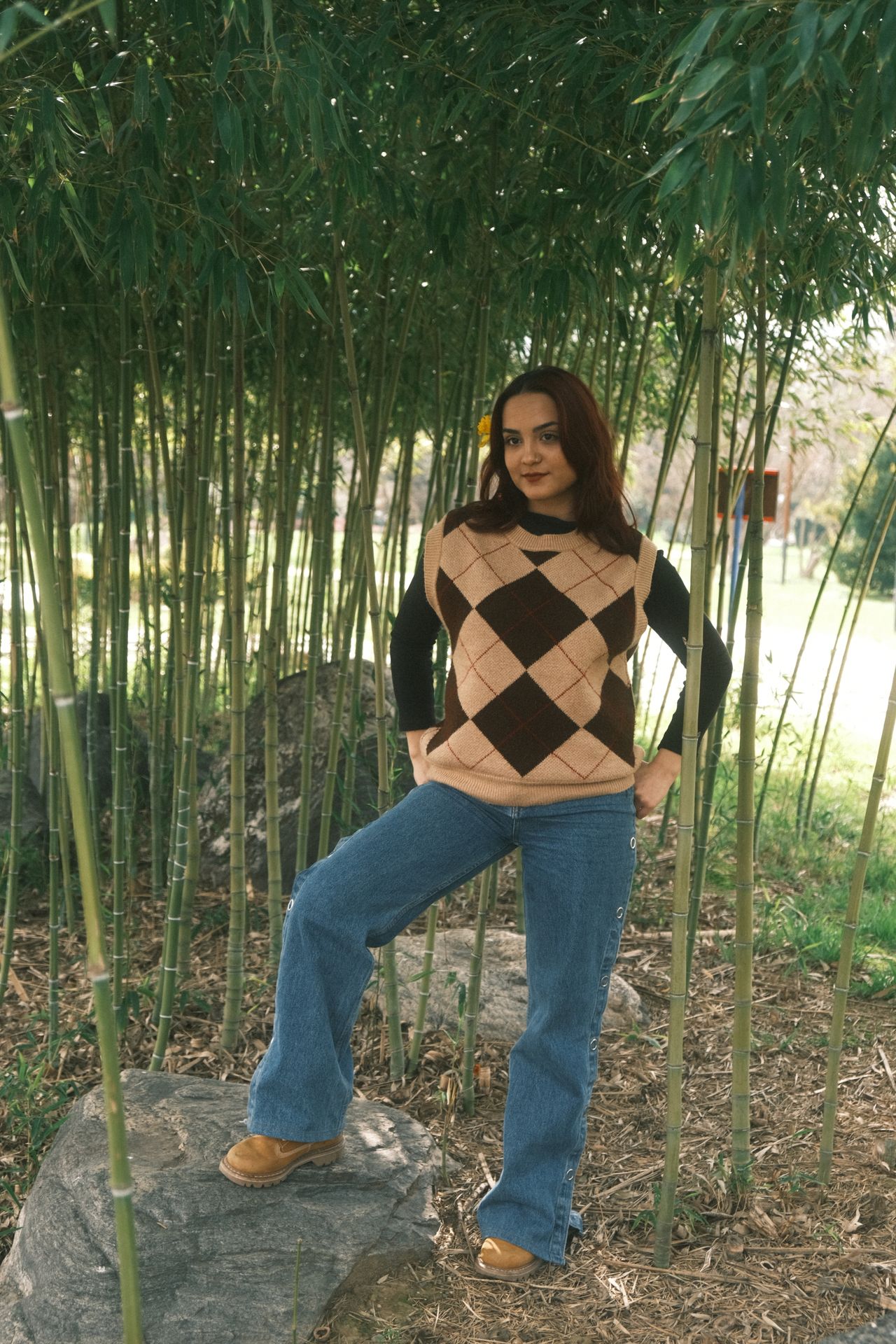 Woman wearing a brown and beige argyle diamond check knit vest with wide leg jeans and boots